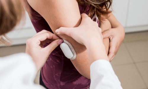 Close-up of health care practitioner's hands applying a CGM sensor on a young woman's right arm