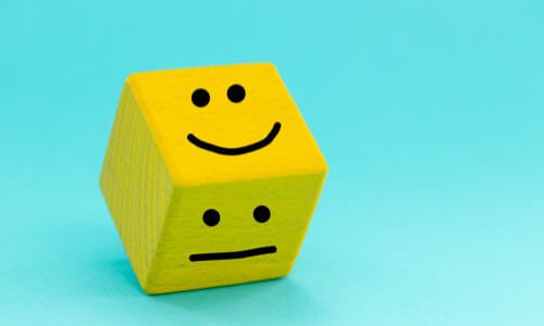 Bright yellow wooden die with black smiley face on top & neutral face on the side