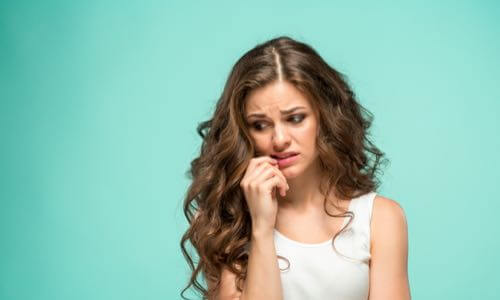 Young woman with long wavy hair touches her lip & looks down with a worried expression on her face