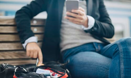 Person sitting on bench outdoors pointing at open diabetes case with insulin pens laying on bench