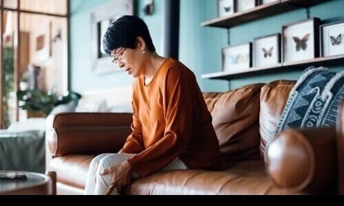 Woman sitting on a sofa looking down as she's massaging her leg