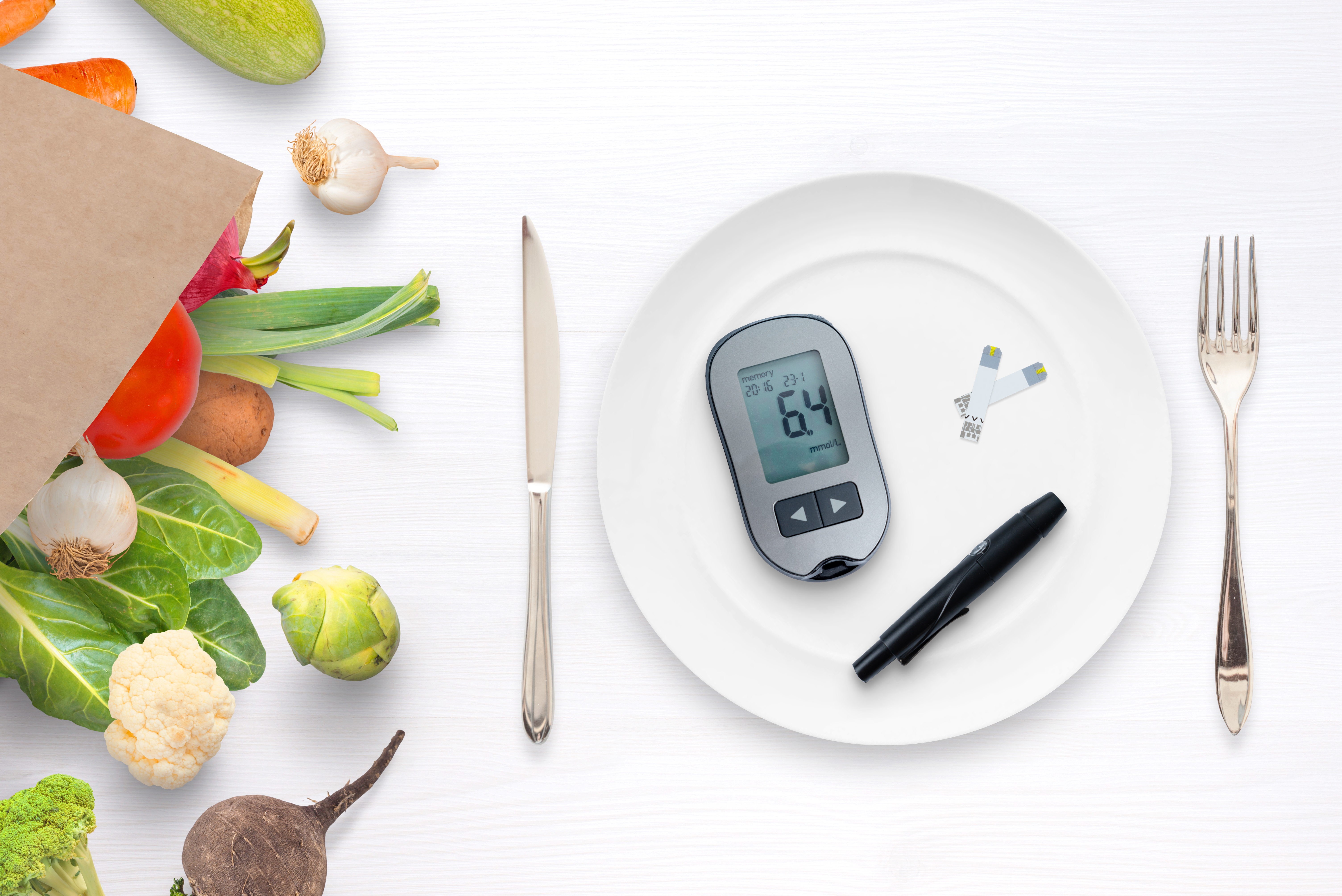 Grocery bag containing produce next to a plate on table with blood glucose monitor, lancing device & test strips on it