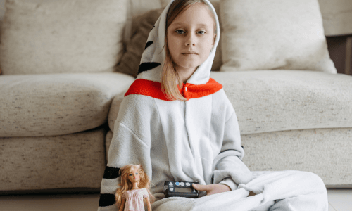 Young girl sitting on the floor in front of a sofa with a Barbie doll in hand & an insulin pump on her lap