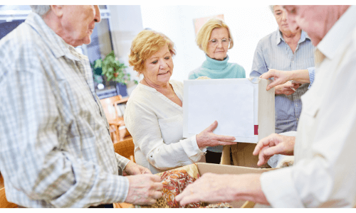 A group of male & female seniors opening a box & viewing its contents