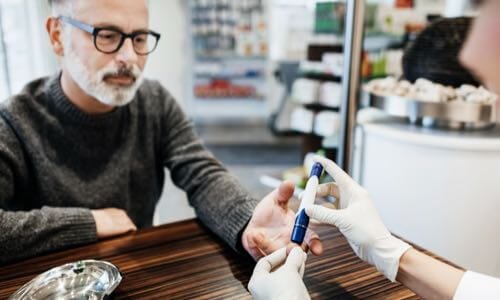 Senior male at pharmacy counter reaching out to pharmacist holding an insulin pen with gloved hands