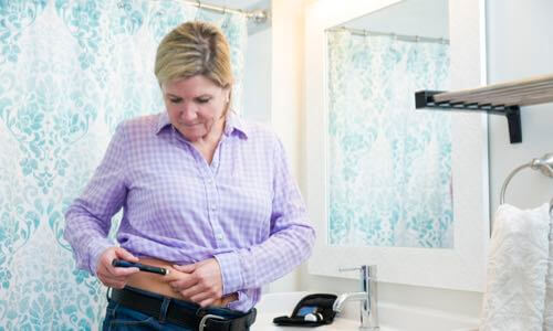 Woman standing at a restroom sink & injecting insulin into her abdomen