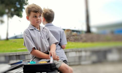 Young boy sitting outside with an open diabetes case at his side & another boy behind him looking away