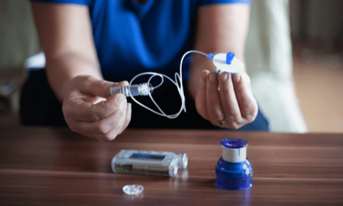 Close-up of female hands holding an infusion set & an insulin pump laying on the table