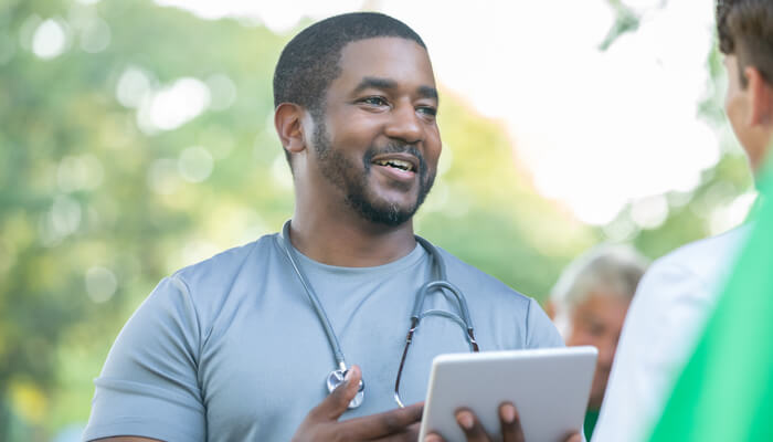 Male health care professional with a computer tablet speaking to a patient outdoors
