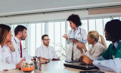 A diverse mix of young health care professionals speaking & listening at a conference room table