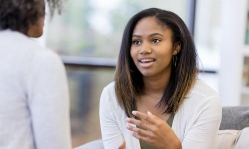 Young diverse woman sitting & speaking with another diverse woman facing her